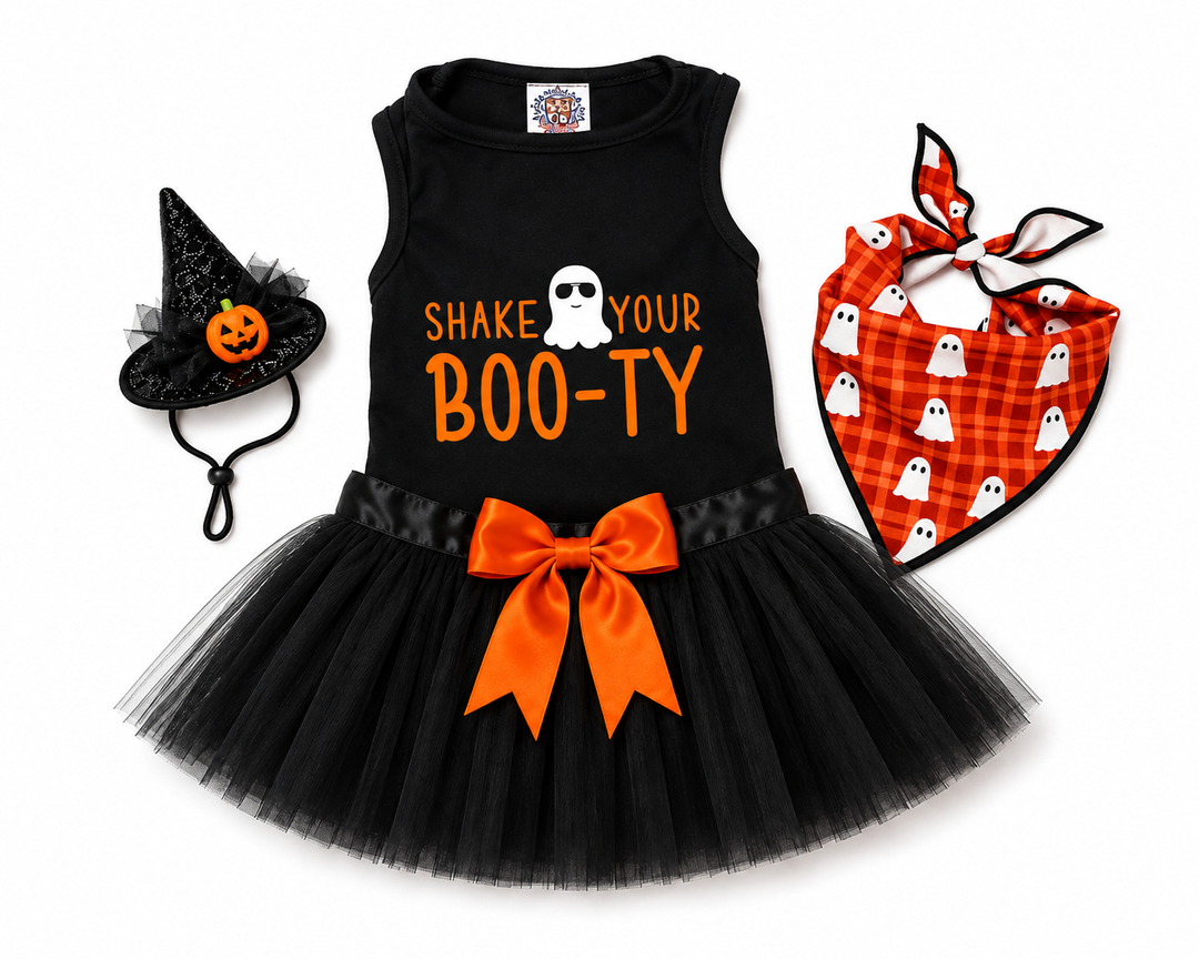 A girl's dog Halloween costume set on a white background, featuring a black sleeveless tutu dress with 'SHAKE YOUR BOO-TY' text and a large orange bow, a black witch hat with a pumpkin face, and an orange plaid bandana with white ghost prints.